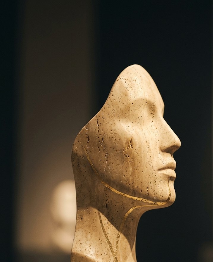Escultura de rosto em travertino com veios de ouro — símbolo do equilíbrio com critério